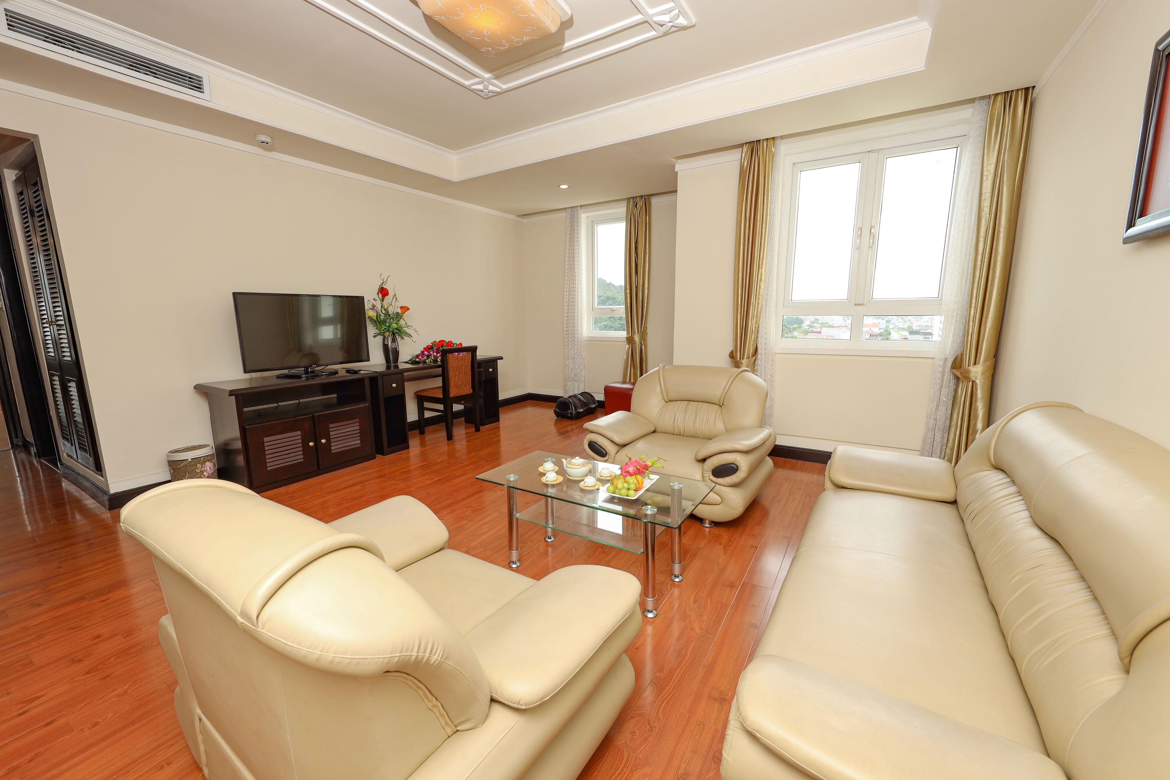 A living room with a sofa, armchair, glass coffee table, TV, and a small cabinet.