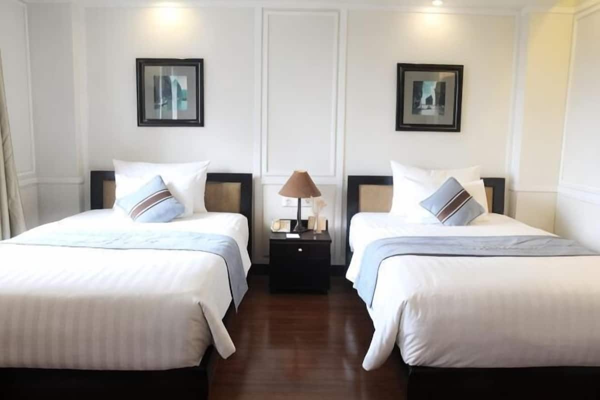 Een hotelkamer met twee bedden, een nachtkastje met een lamp en ingelijste foto's aan de muur.