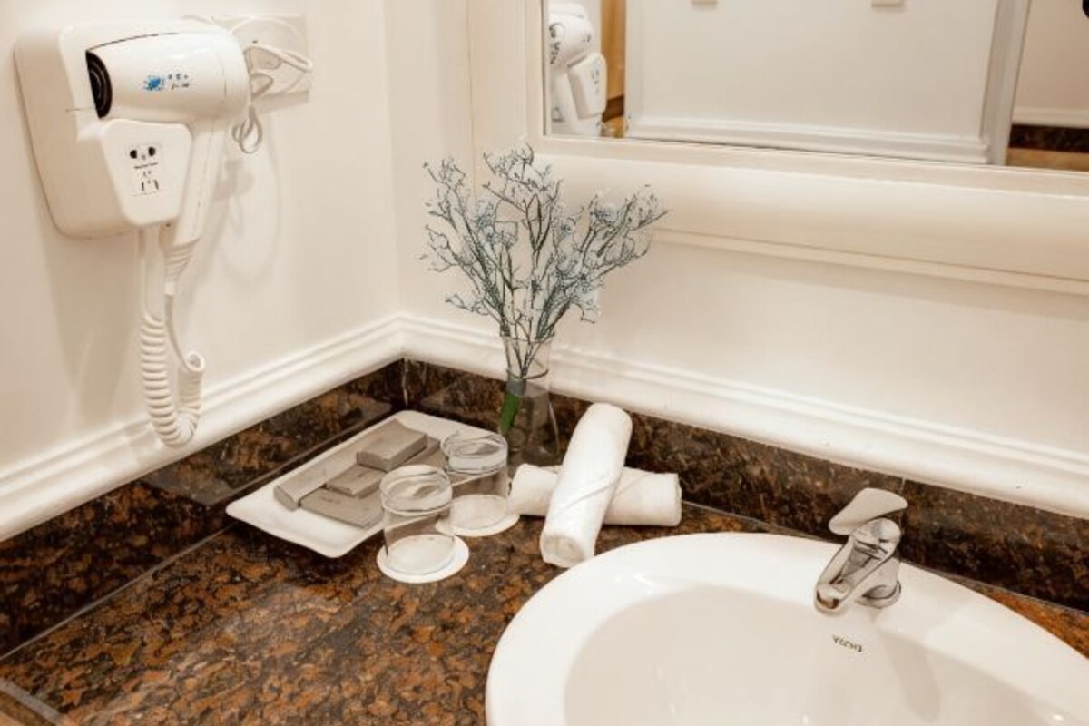 Un baño con secador de pelo, un pequeño florero con flores secas, un lavabo y un espejo.