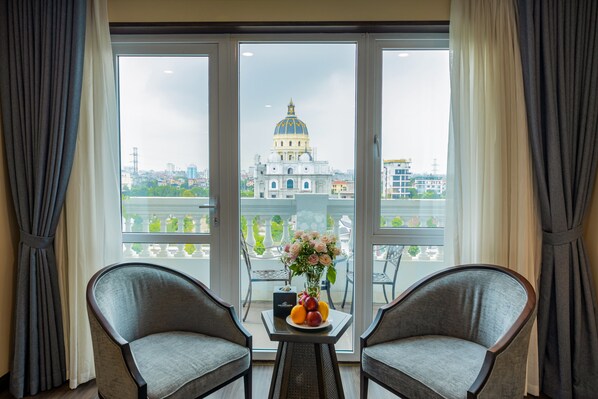 Una habitación con dos sillones, una mesita con fruteros y flores, y vista a un edificio grande con cúpula a través de un puerta de vidrio.