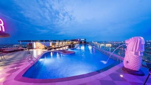 A rooftop pool area with a view of the city at dusk, a bar area, and a statue.
