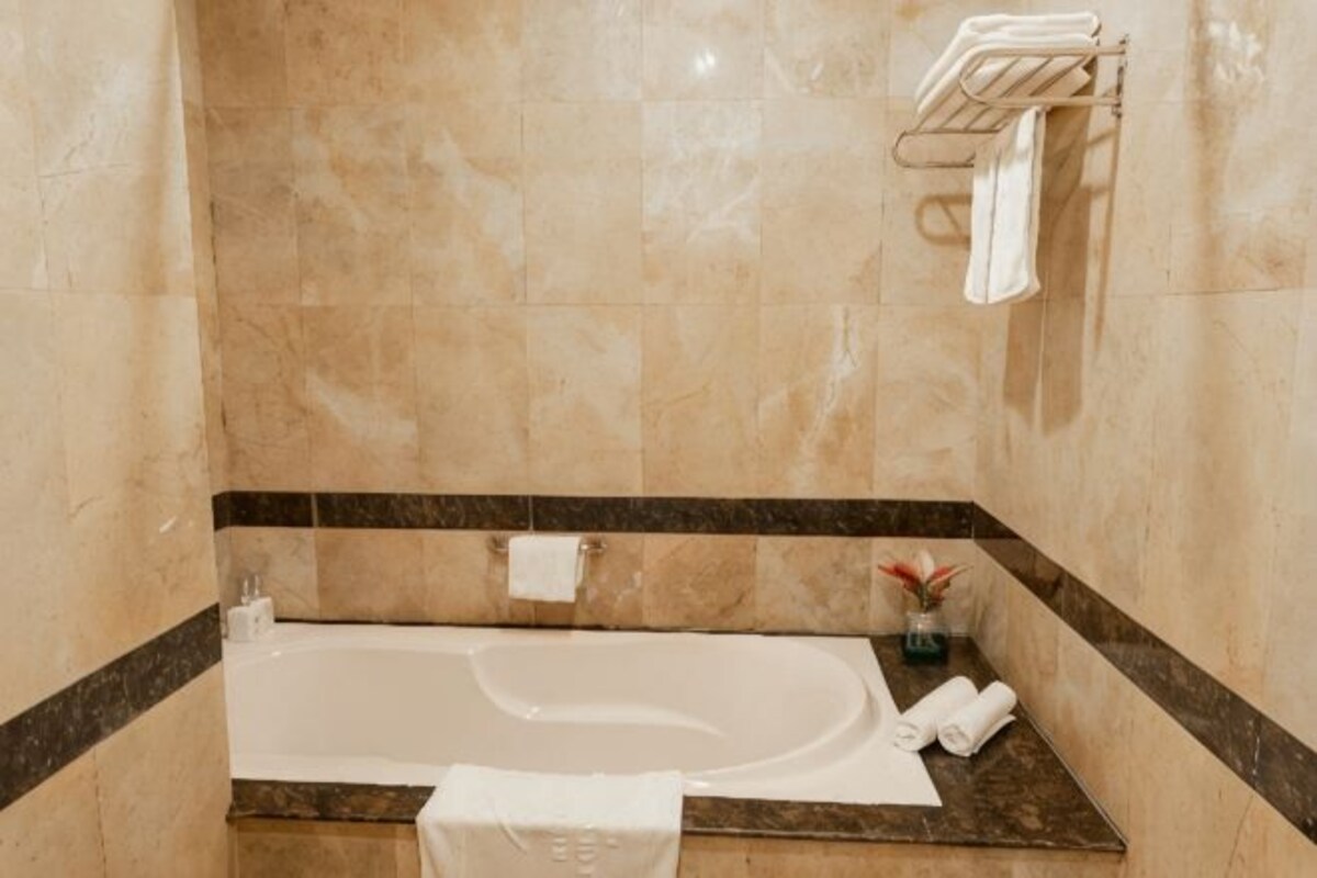 Un baño con bañera, toallero y un pequeño florero con una flor.