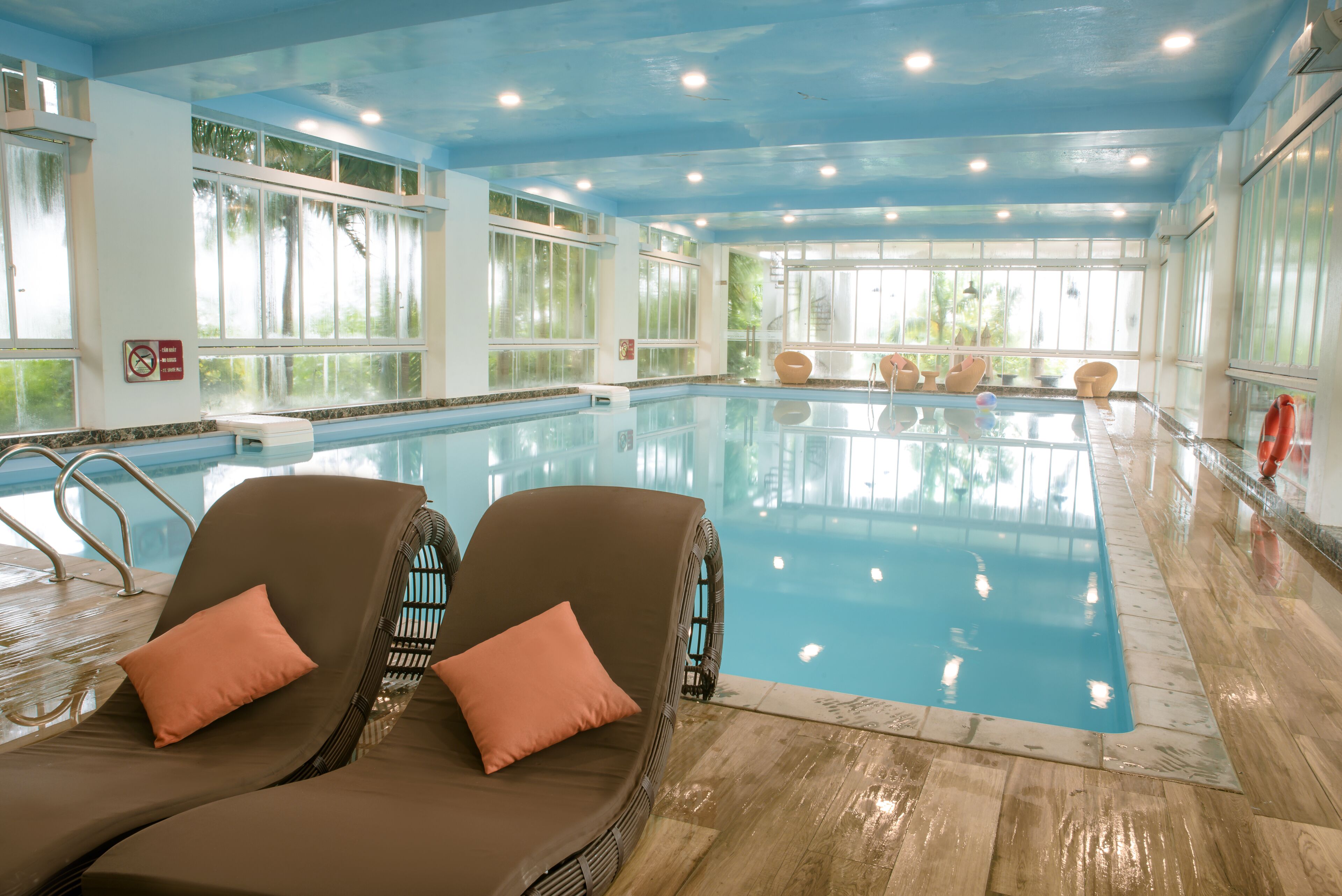An indoor swimming pool with lounge chairs and a clear view of the outside.