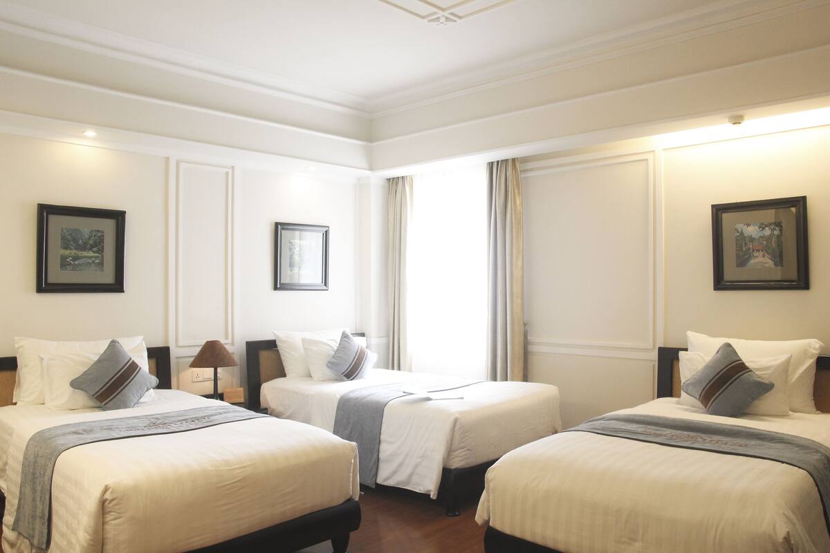 Een hotelkamer met twee eenpersoonsbedden, een groot raam met gordijnen en afbeeldingen in lijsten aan de muren.