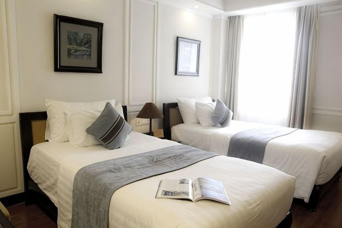 Une chambre d’hôtel avec deux lits, une table de chevet, une lampe et un tableau encadré au mur.
