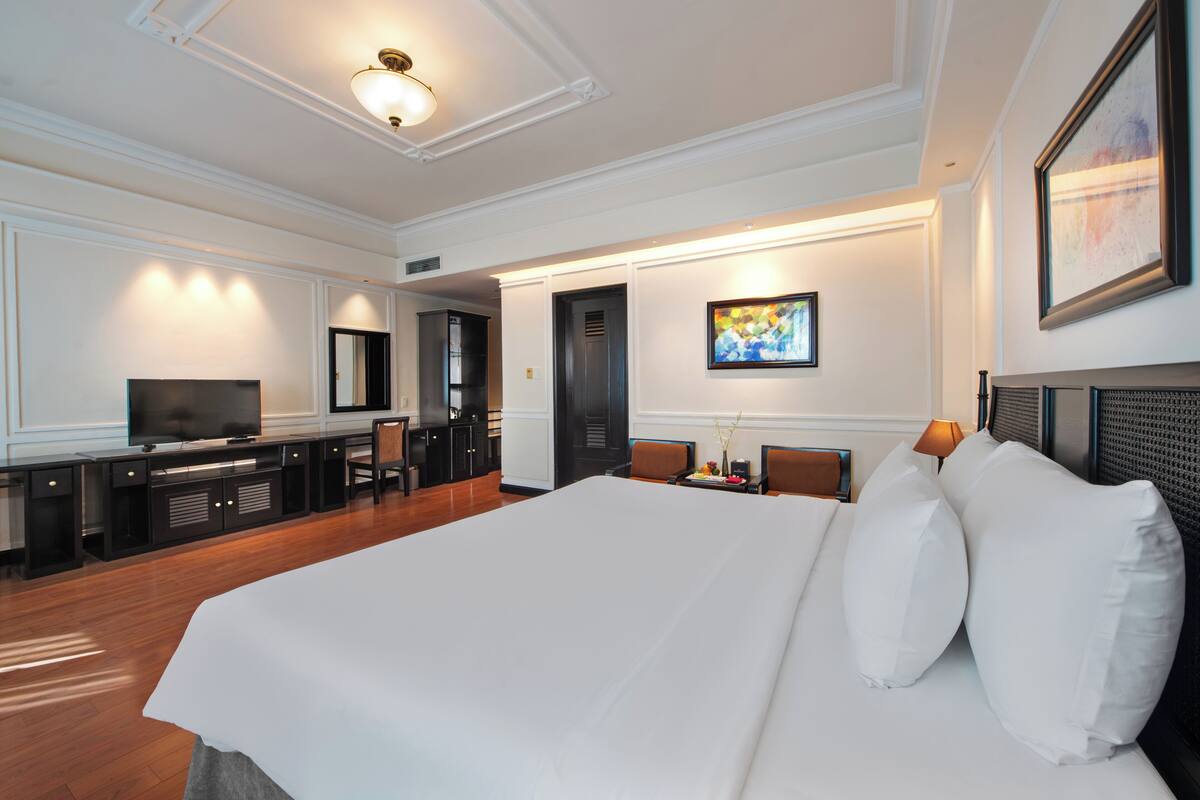 Een hotelkamer met een groot bed, een bureau met een computer, een televisie en een schilderij aan de muur.