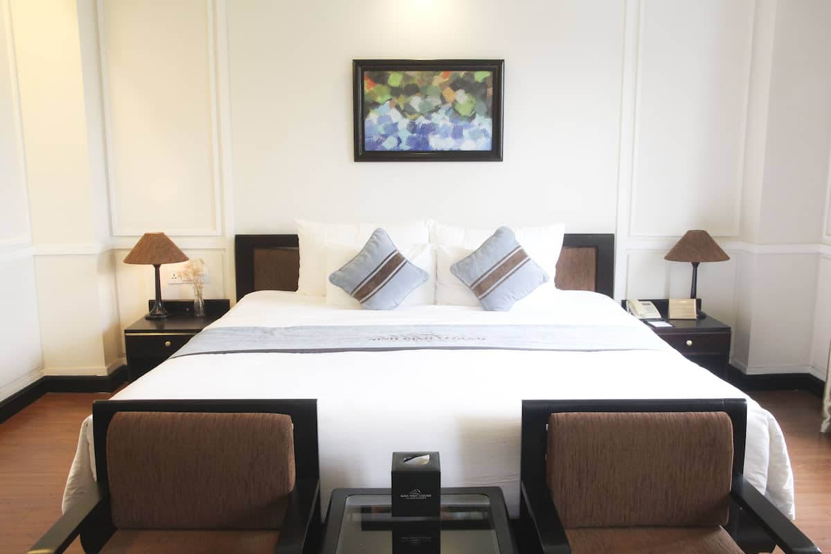 Hotelkamer met een groot bed, twee nachtkastjes, een lijst met abstract schilderij en een glazen tafel met een doos erop.