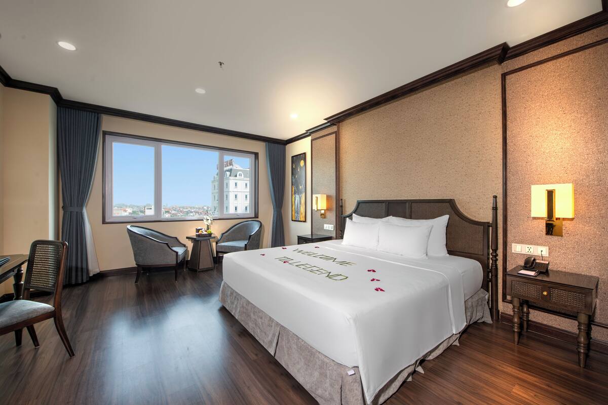 Een hotelkamer met een groot bed, een bureau, twee stoelen, een nachtkastje en een raam met uitzicht over de stad.