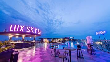 Un bar en la azotea con piscina, taburetes de bar y un letrero de neón que dice "LUX SKY BAR".