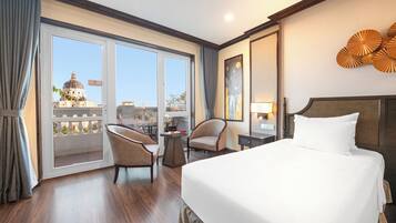 A hotel room with a large bed, two armchairs, a small table, and a view of a dome building through a sliding door.