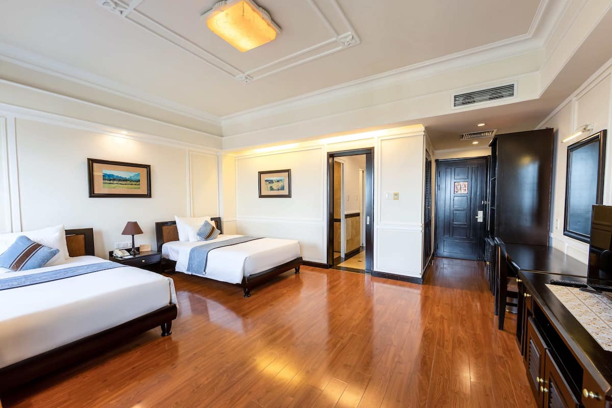 Een hotelkamer met twee bedden, een televisie, een bureau en een deur naar een gang.