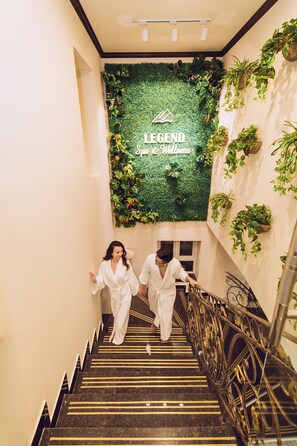 Una escalera con pared verde y plantas que conduce a un espacio con un cartel que dice 'Legend Spa & Wellness'.