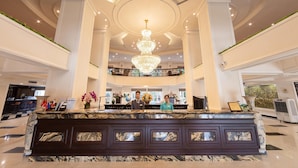 A grand lobby with a marble reception desk, a large chandelier, and a high ceiling.