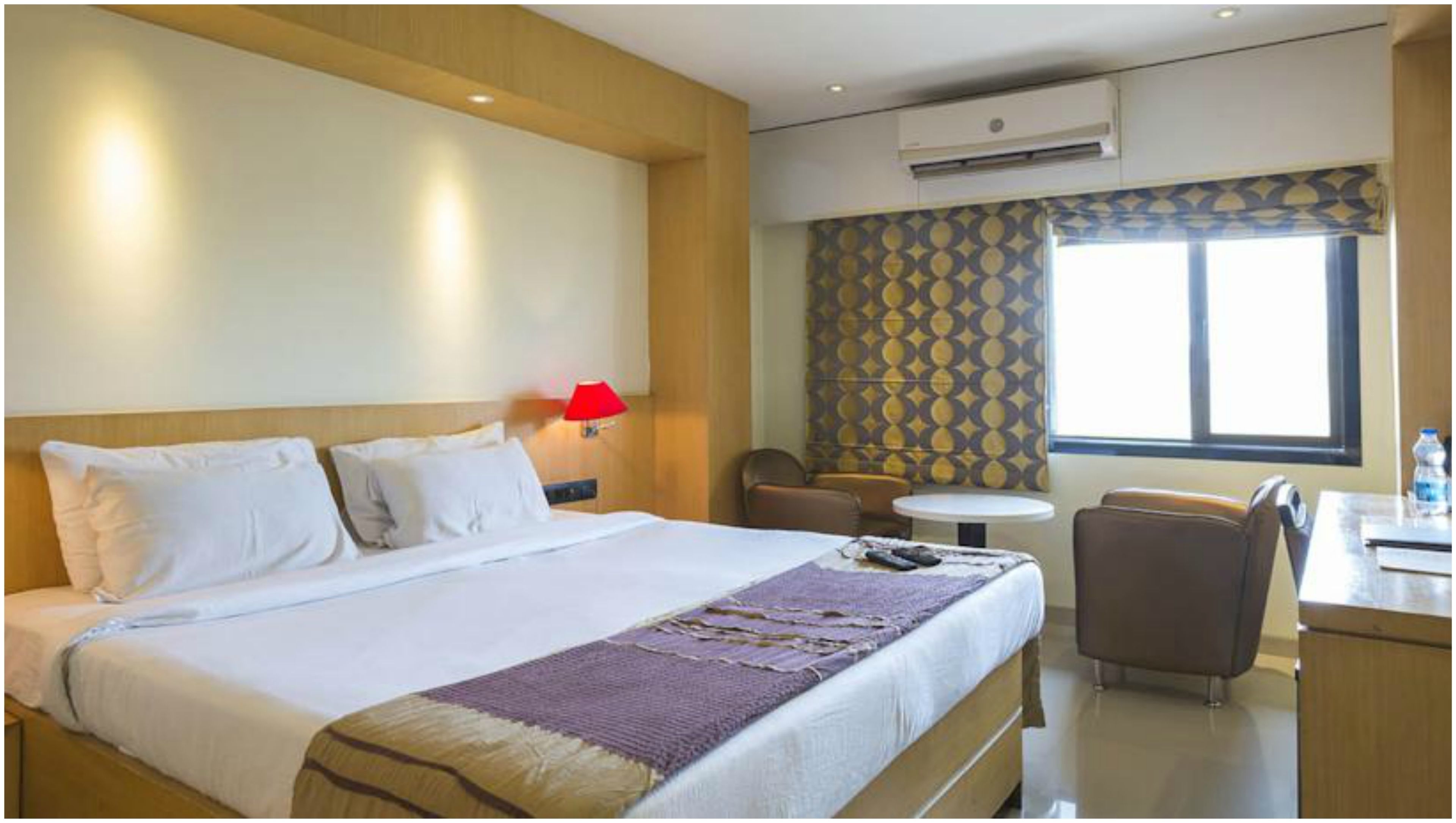 Habitación de hotel con cama, escritorio, silla, mesita y ventana.