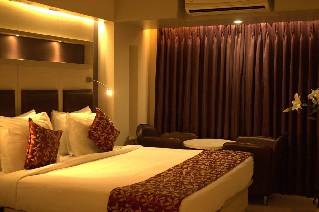 Una habitación de hotel con una cama grande, un escritorio, dos sillas, una mesita y una cortina.