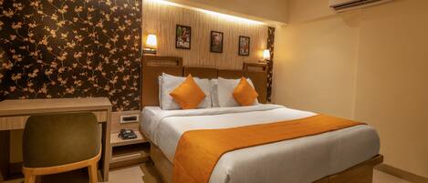 Habitación de hotel con cama, escritorio, silla y unidad de aire acondicionado en la pared.