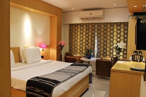 Habitación de hotel con cama, escritorio, silla, mesita y un jarrón con flores.