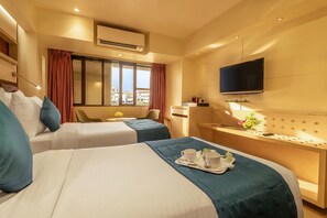 Habitación de hotel con dos camas, televisión, escritorio y ventana con cortinas.
