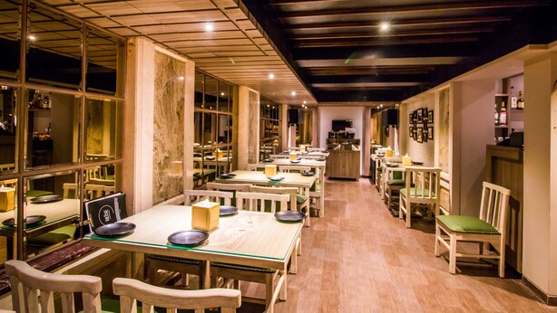 A restaurant with wooden tables and chairs, a marble column, and a dark ceiling. - Hotel Oriental Aster - Mumbai International Airport (Mumbai)