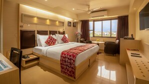 A hotel room with a bed, bedside table, chair, desk, and a large window with a city view. - Hotel Oriental Aster - Mumbai International Airport (Mumbai)