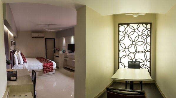 Una habitación de hotel con cama, mesita de noche y escritorio con silla. Hay una ventana con un panel decorativo.