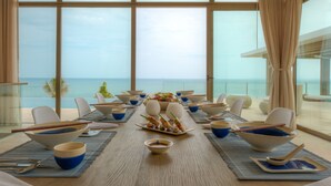 Comedor con vistas al océano, que incluye una mesa larga dispuesta con cuencos, palillos y un plato de comida en el centro.