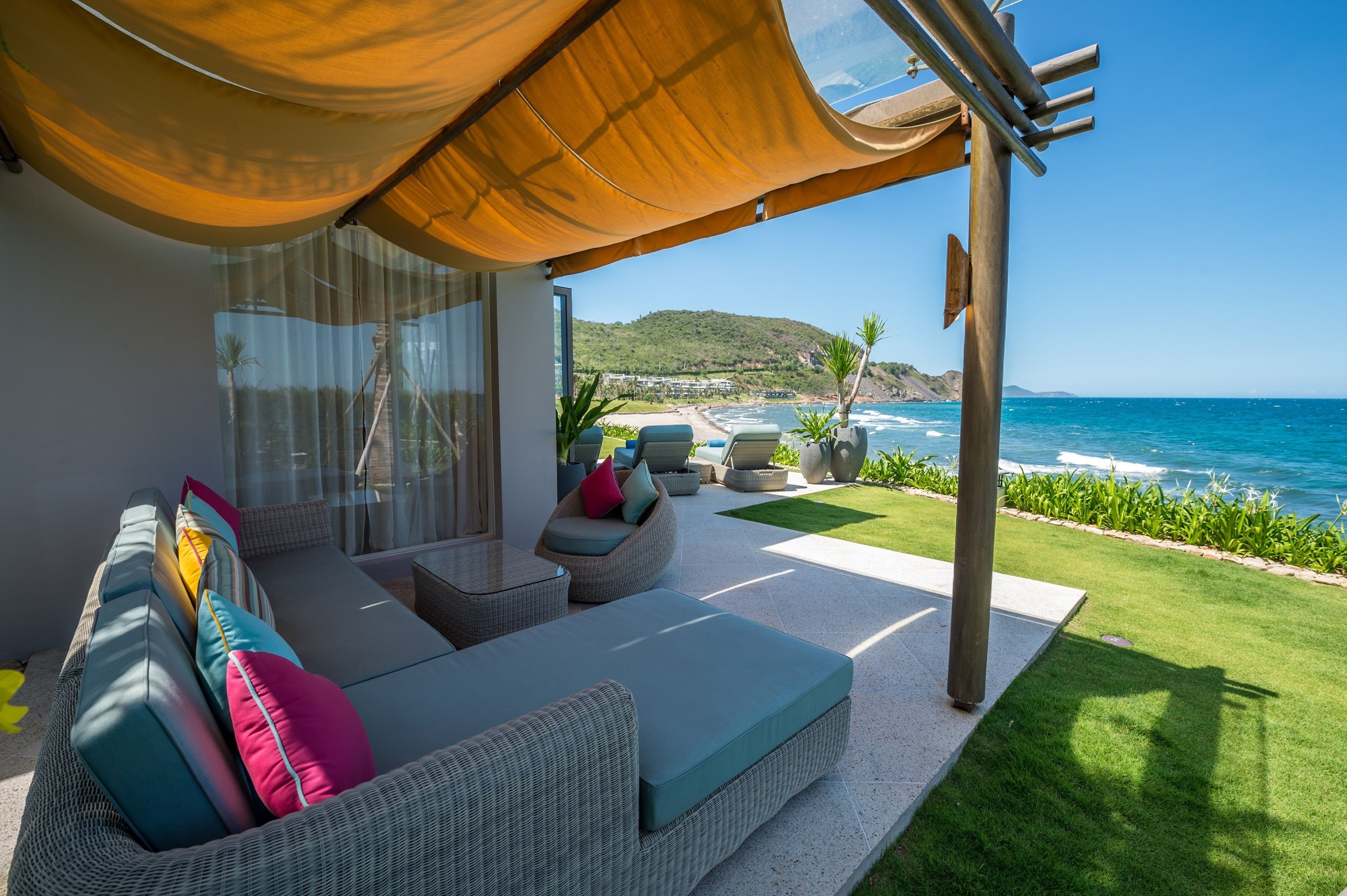 Un espacio de estar techado al aire libre con muebles de mimbre y cojines, con vista a una playa y al océano.