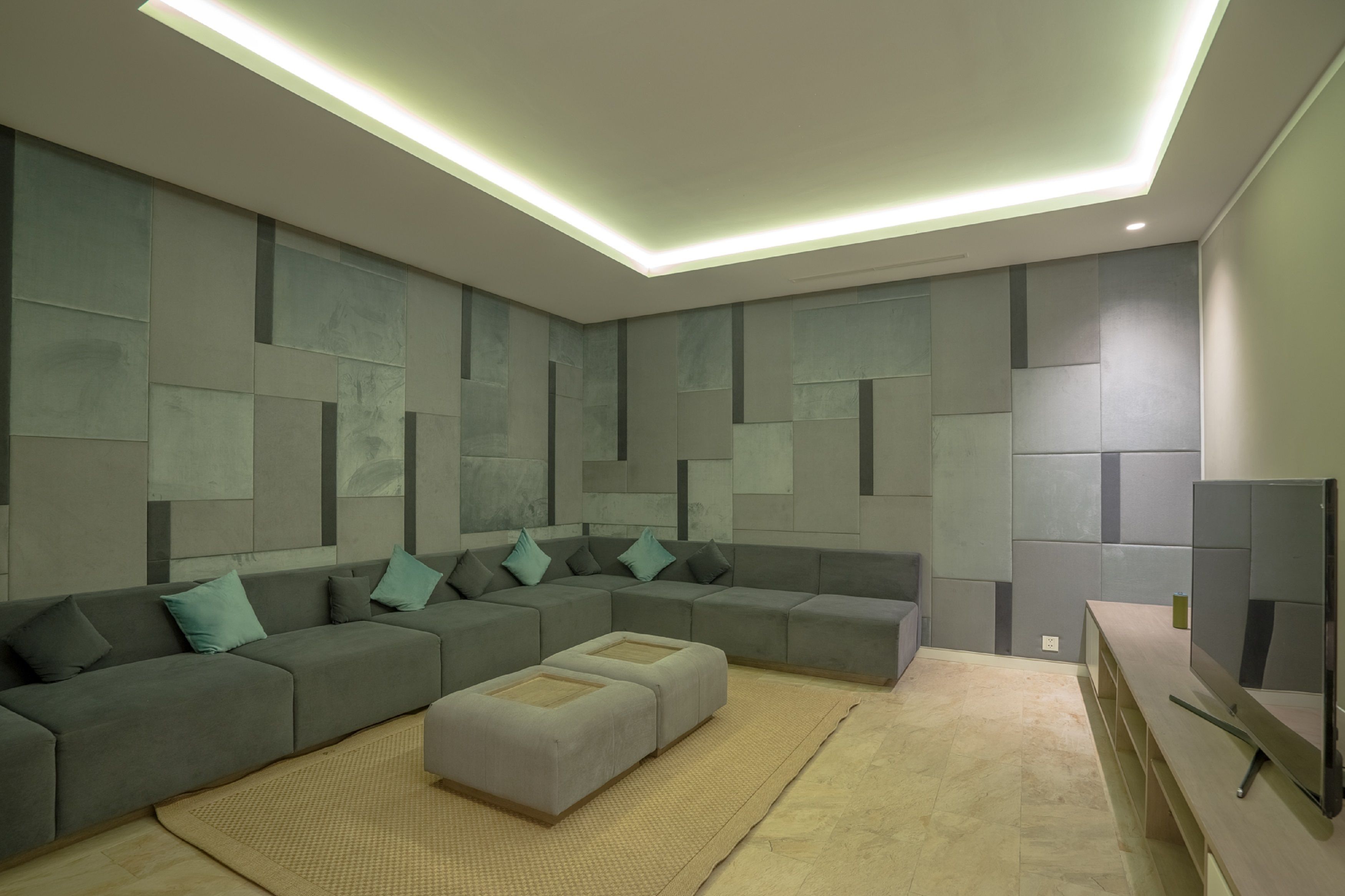 Ein modernes Wohnzimmer mit Ecksofa, Ottoman, Flachbildfernseher und Einbau-Deckenleuchten.