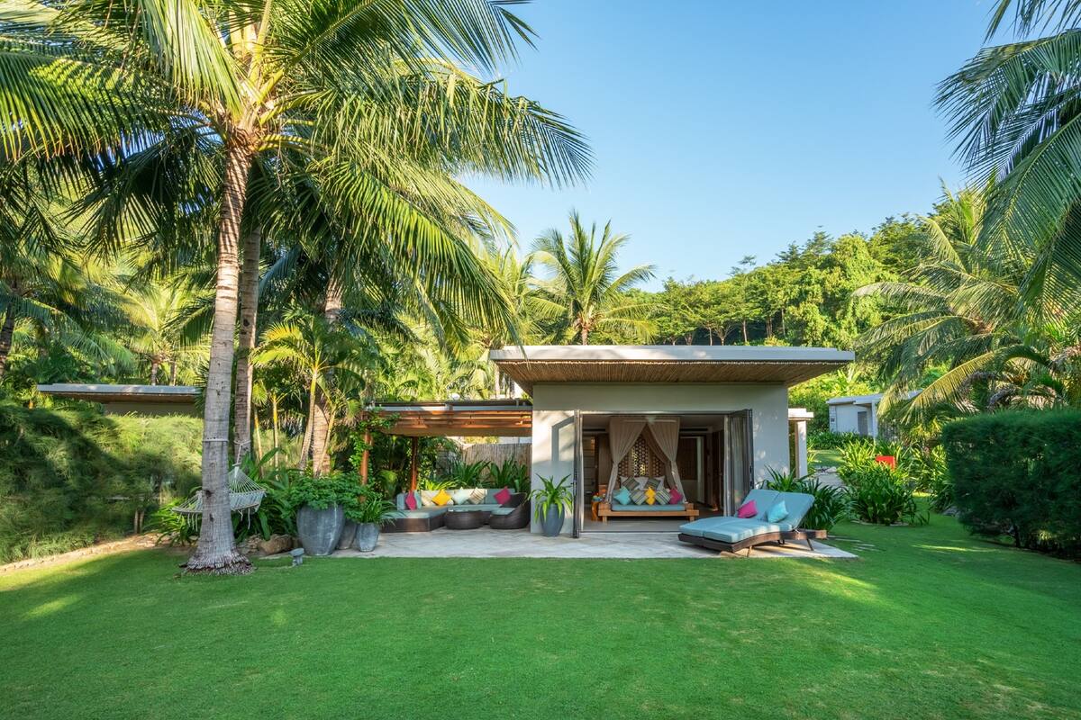 A modern house with a covered patio, a hammock, and a seating area with cushions.