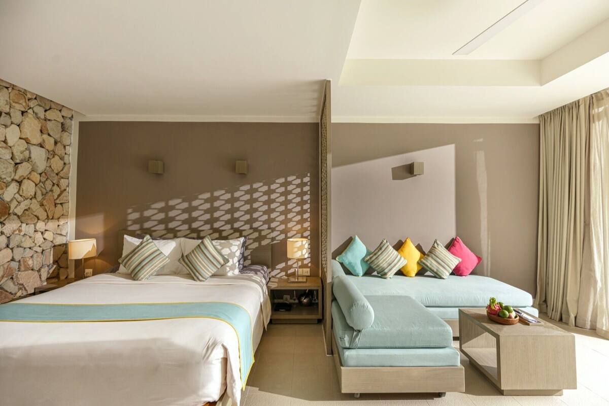 A hotel room with two beds, a sofa, a small table, and a stone wall.