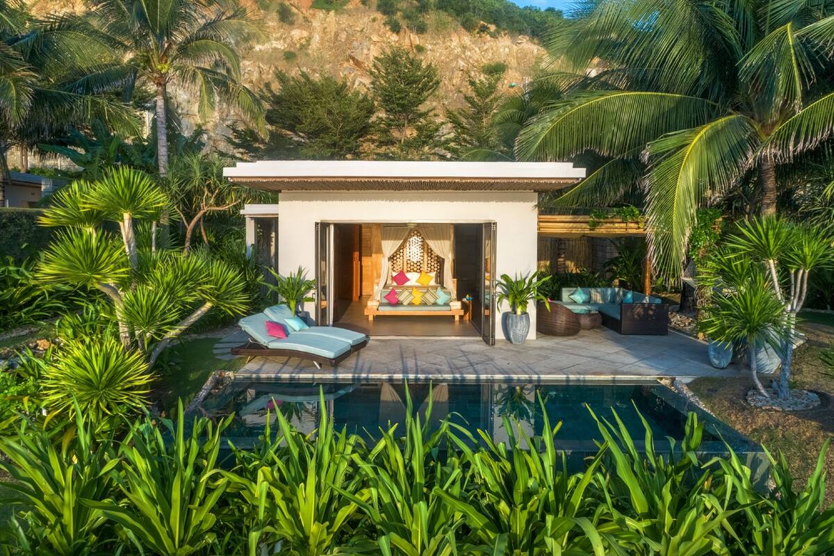 A modern villa with a pool, surrounded by lush greenery and palm trees.