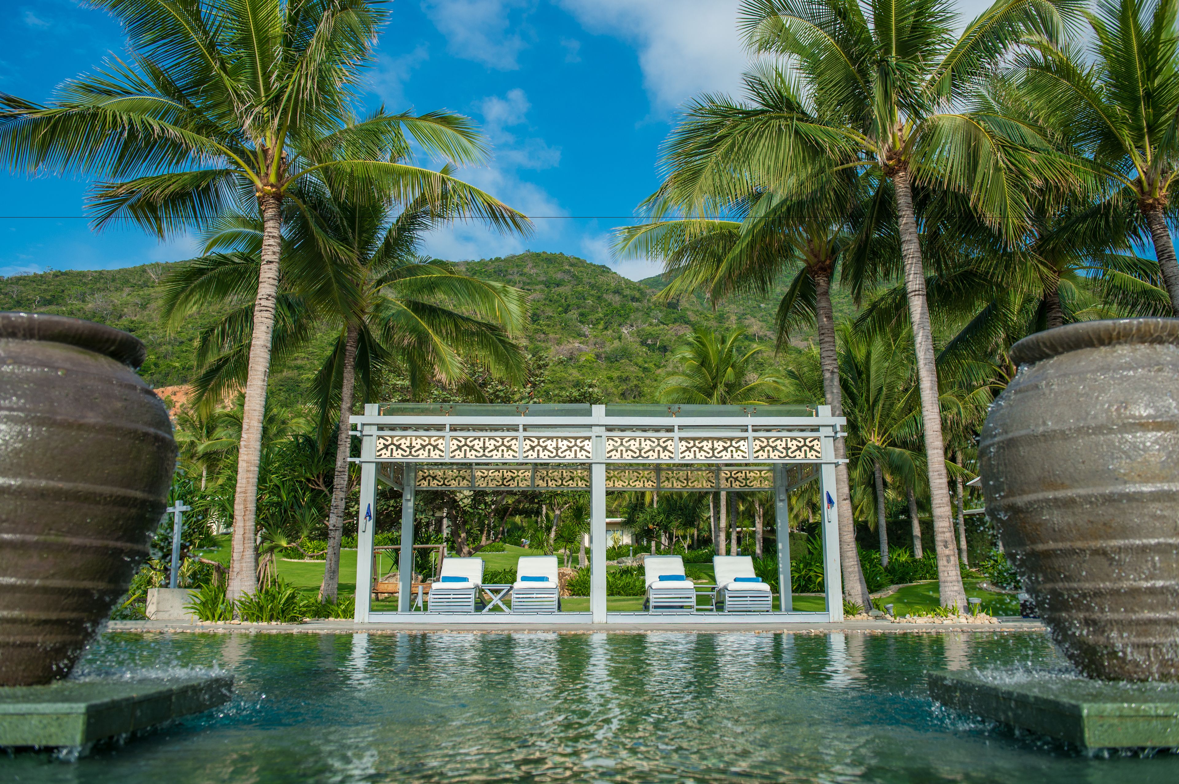 A pool area with lounge chairs, palm trees, and a gazebo structure.