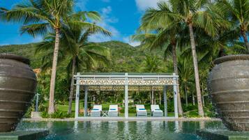 A pool area with lounge chairs, palm trees, and a gazebo structure.