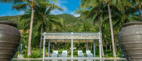 A pool area with lounge chairs, palm trees, and a gazebo structure.
