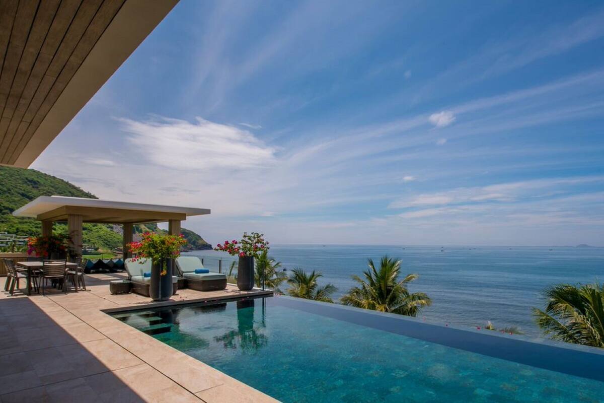 A infinity pool with a view of the ocean and a covered seating area with chairs and tables.