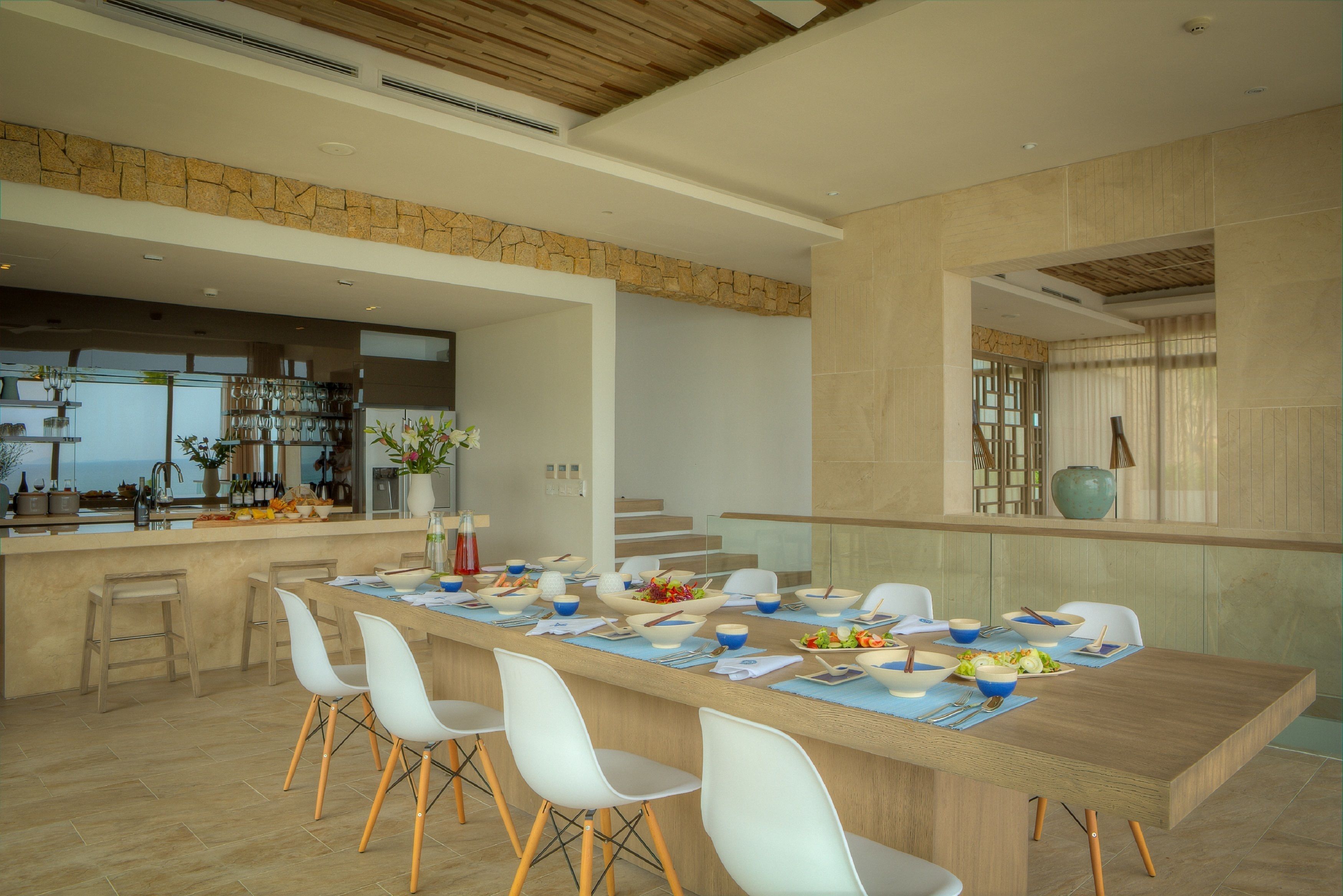Une cuisine moderne avec un grand îlot central, des chaises blanches et un mur d’accent en pierre.
