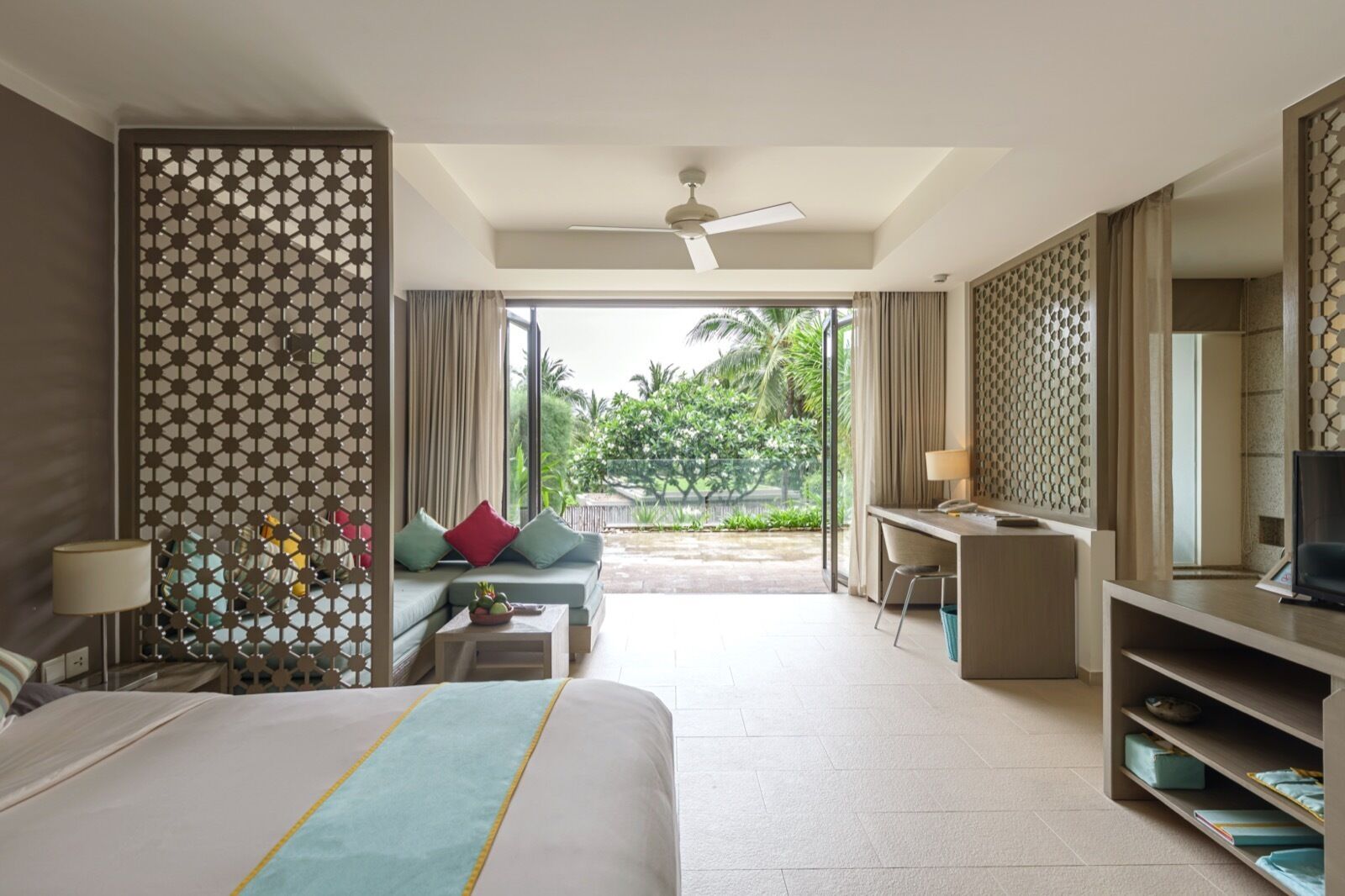 A hotel room with a bed, a desk, a sofa, and a balcony with a view of greenery.