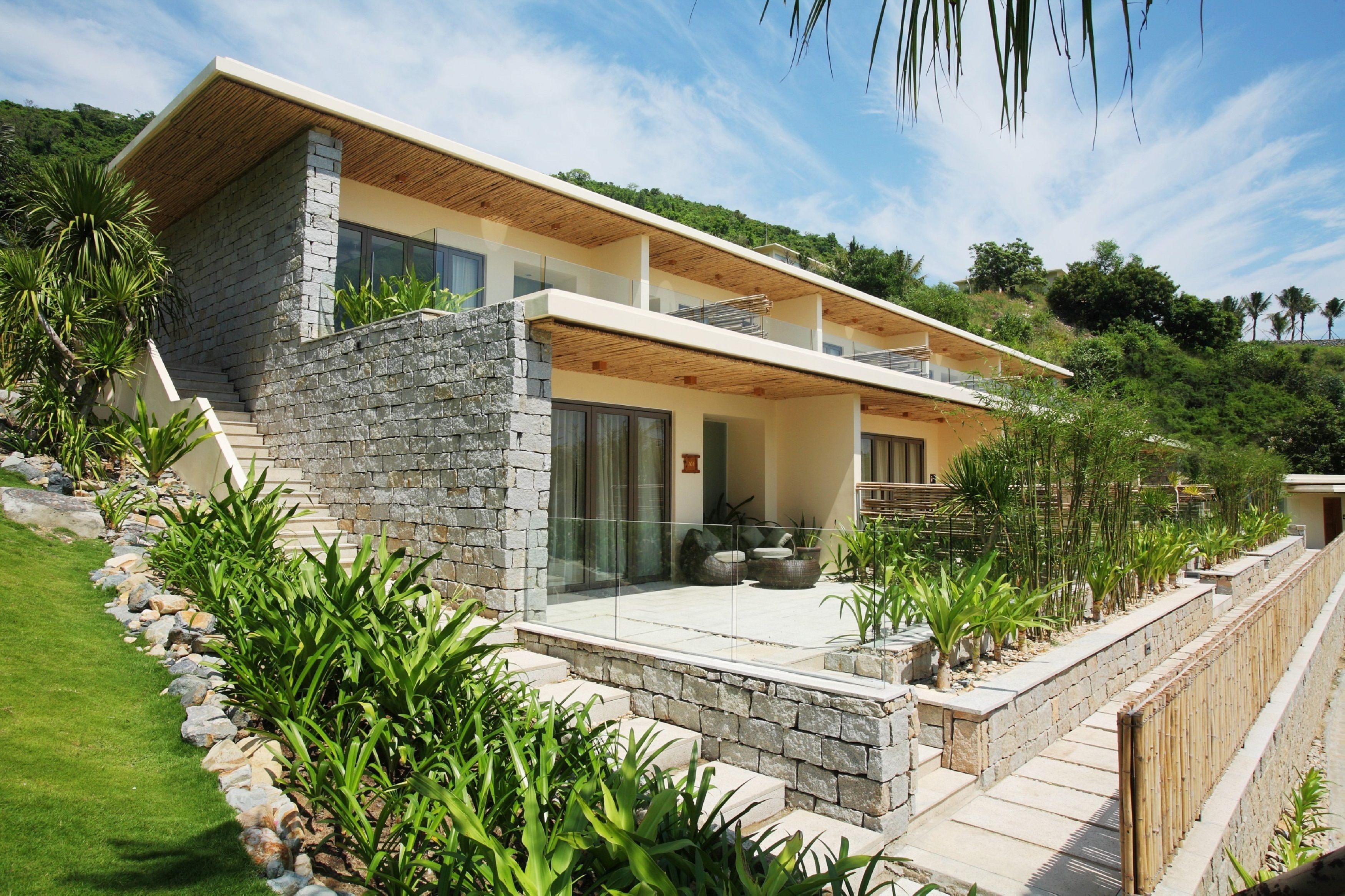 Une maison moderne à deux étages, dotée d’une façade en pierre, de grandes fenêtres et d’un balcon.