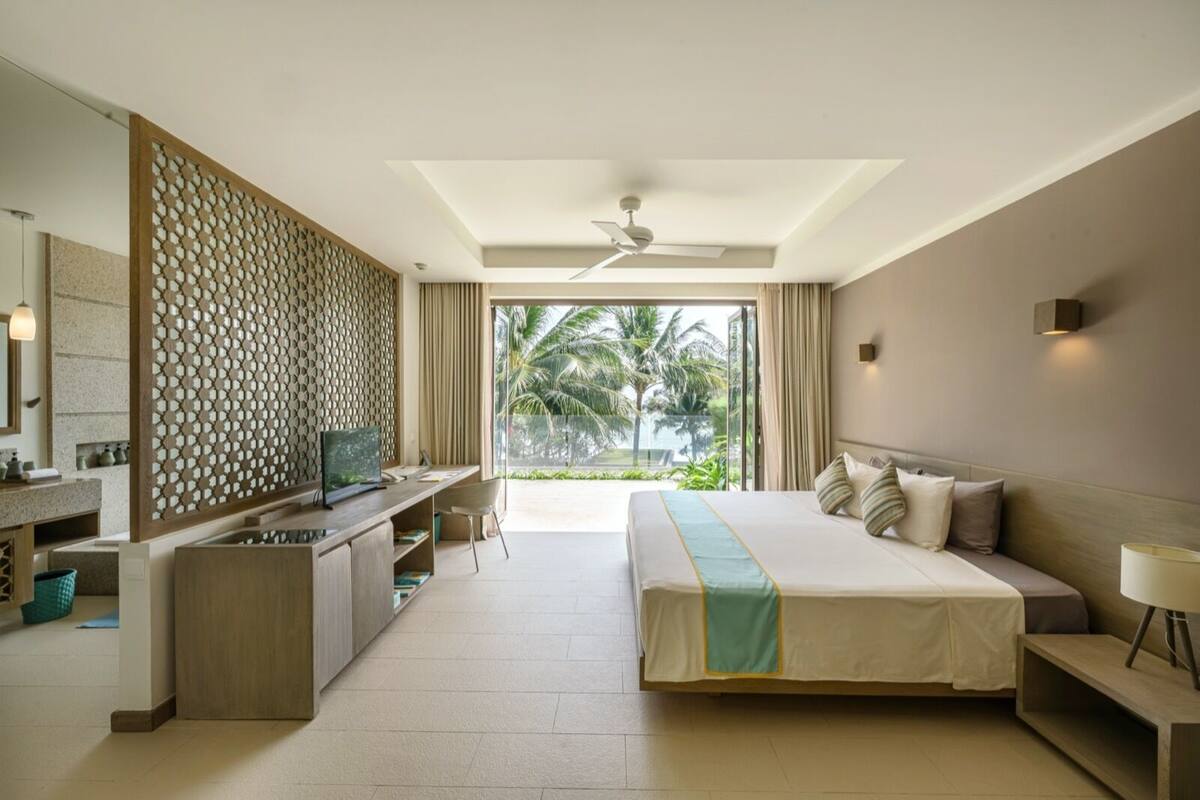 A hotel room with a bed, desk, and a view of palm trees.