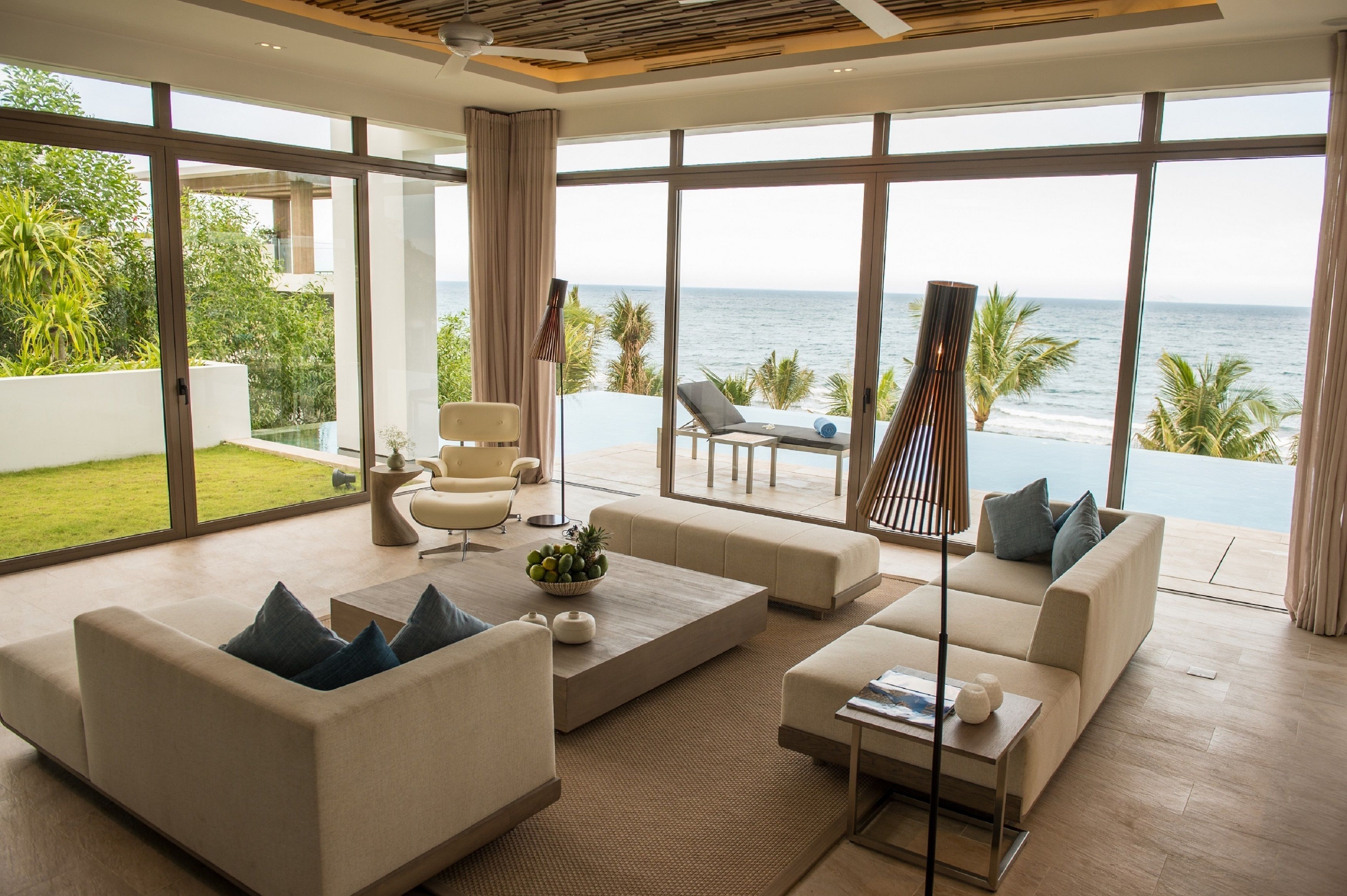 A spacious living area with large windows overlooking a pool and the sea.