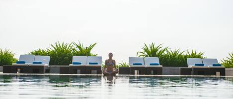 A poolside area with lounge chairs and a person meditating.