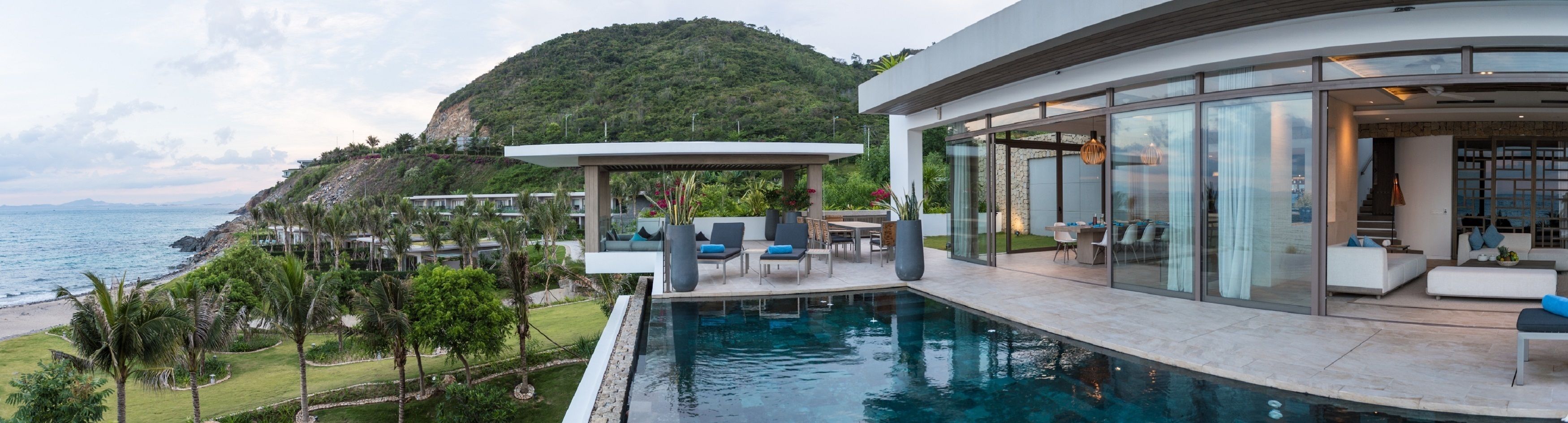 A modern house with a pool, outdoor seating, and a view of the sea and mountains.