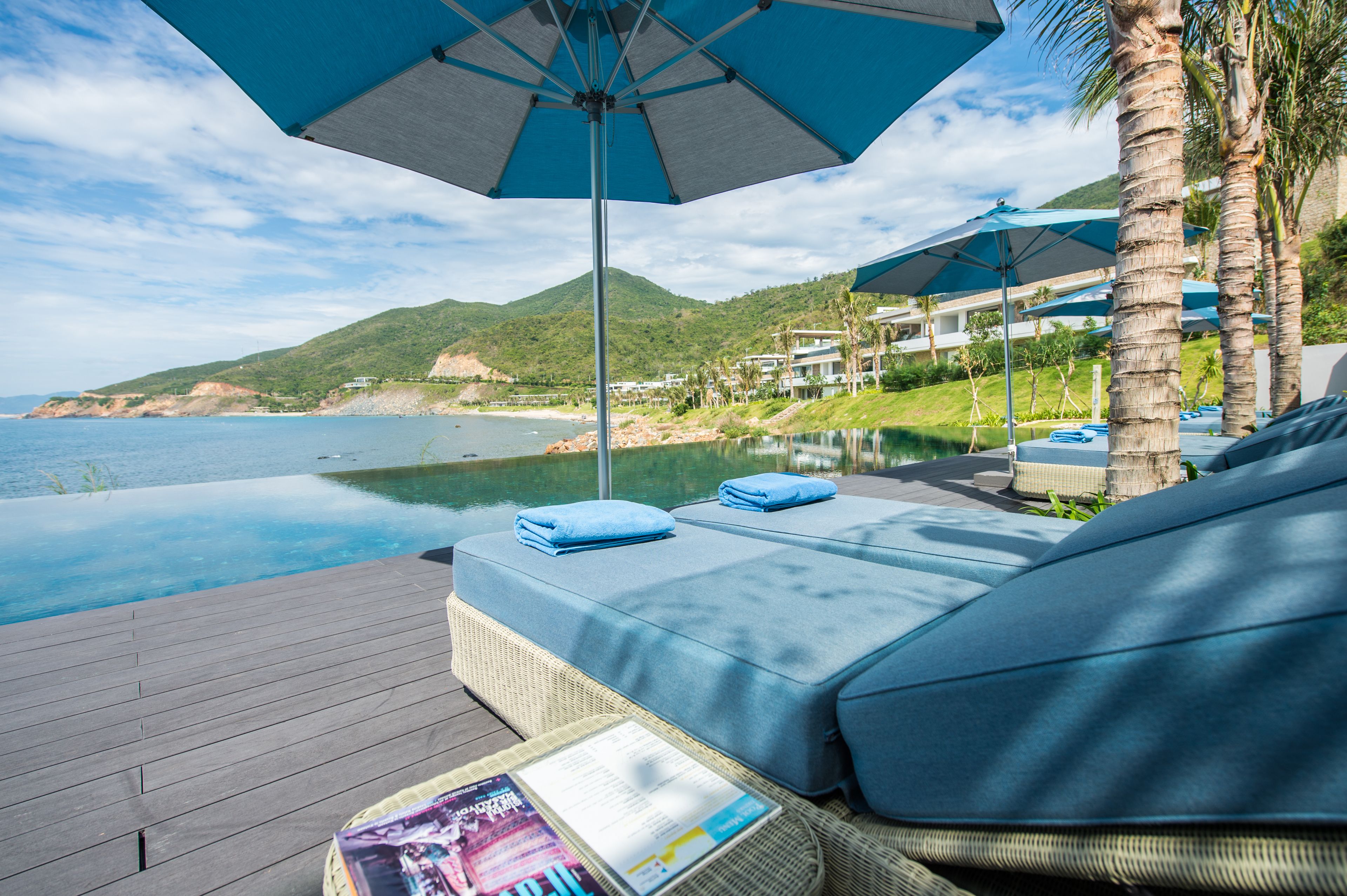 Une terrasse avec une piscine, des chaises longues et des parasols, offrant une vue sur la plage et les montagnes.
