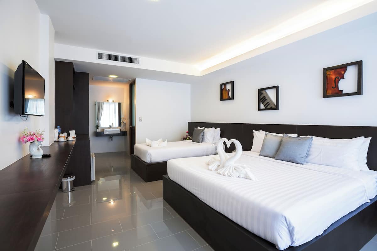 A modern hotel room with two beds, a TV, artwork on the walls, and a bathroom visible through an open door.