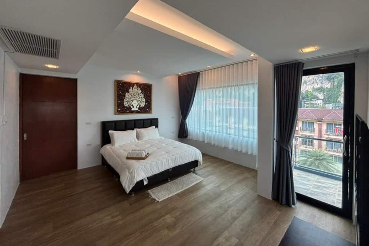 A modern bedroom with a bed, a ceiling light, a window with curtains, and a view of buildings outside.