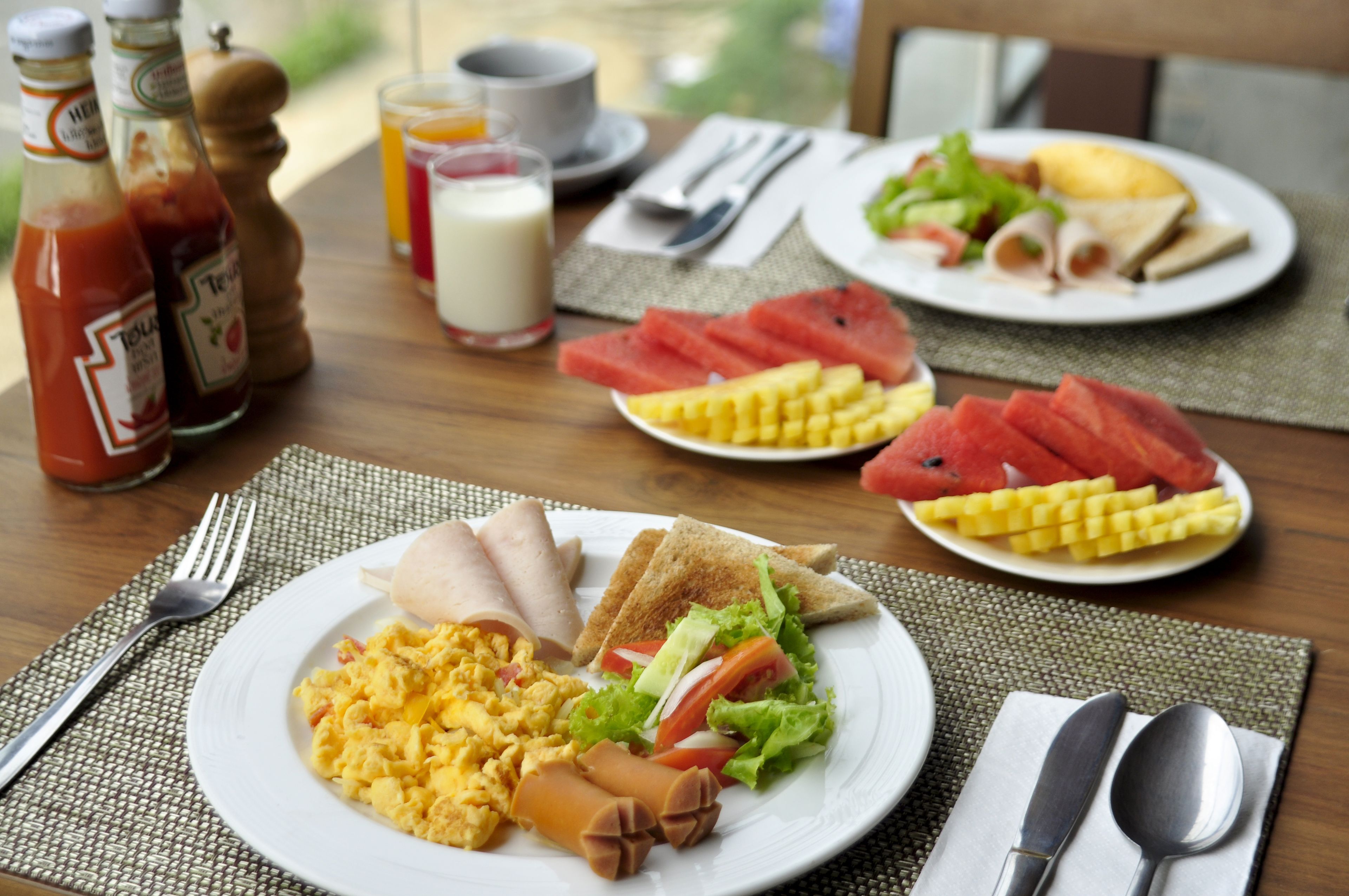 A breakfast setting with plates of eggs, toast, and fruit, along with condiments and utensils on a table.