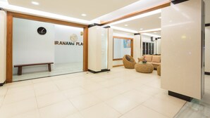 Un lobby moderno con un banco, un mostrador de recepción y una pared con el texto "IRANANG PLA".