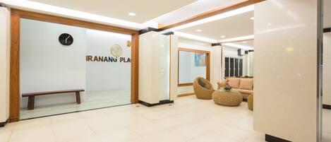 A modern lobby with a bench, a reception desk, and a wall with the text "IRANANG PLA".