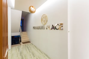 A hallway with a marble floor, a wooden handrail, and a staircase leading to another level. The wall has a sign that reads "PRANANG PLACE" with a decorative emblem above it. - Phranang Place Hotel (Krabi)