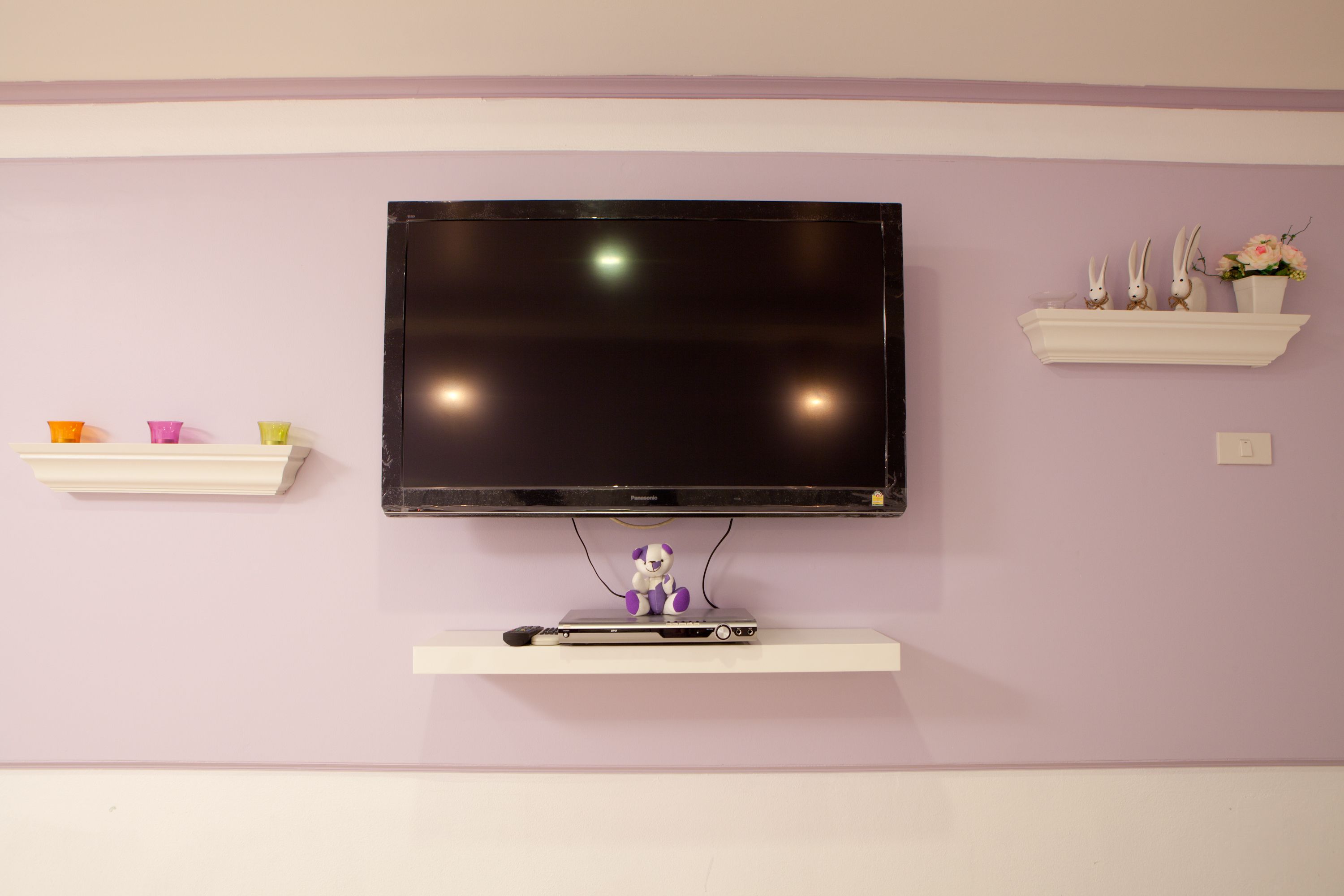 A flat-screen TV mounted on a wall with a white shelf below it.